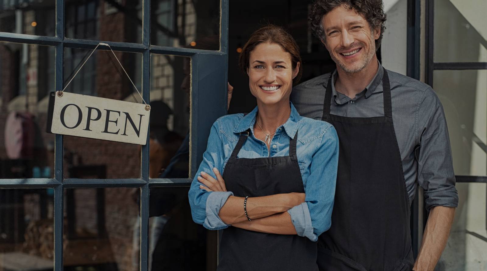 man and women standing in front of a business with an open sign next to them