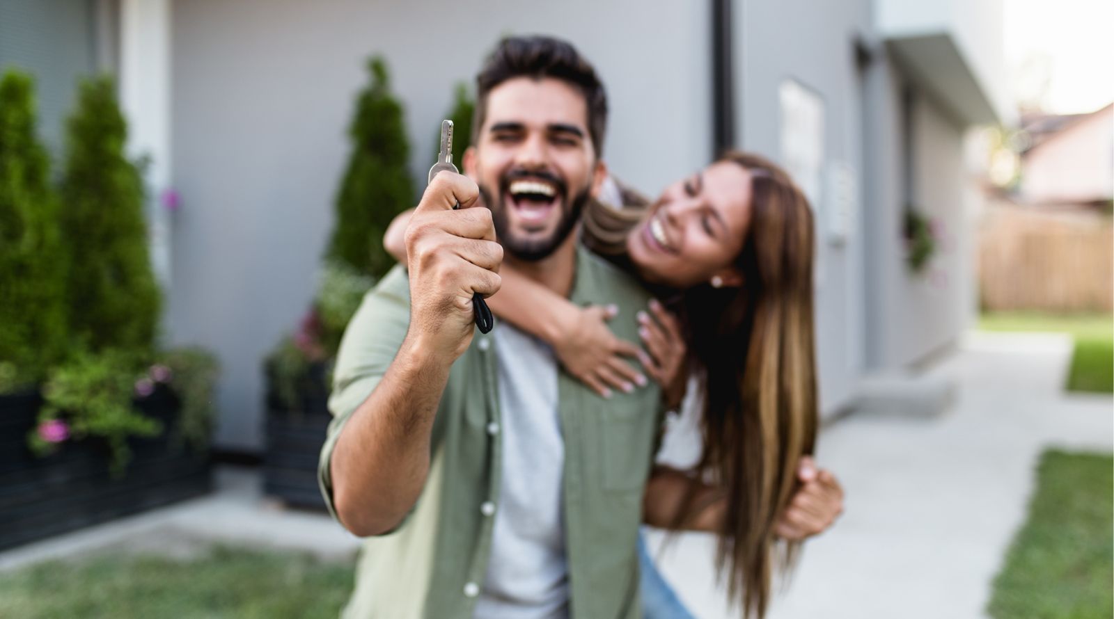 Couple just bought house male smiling holding a key being hugged by a woman